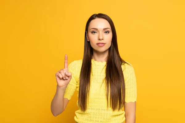 Attractive girl pointing with finger on yellow background — Stock Photo