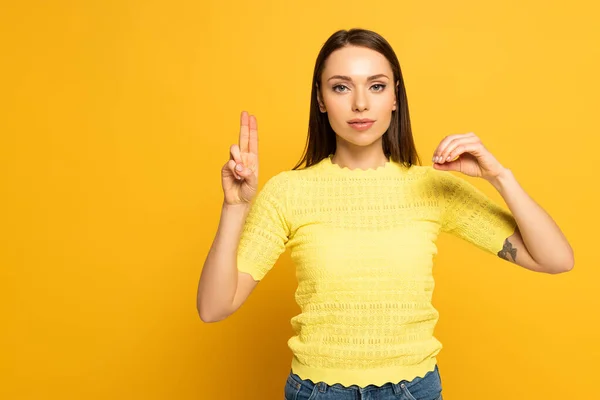 Donna che mostra lettere in lingua sorda e muta su sfondo giallo — Foto stock