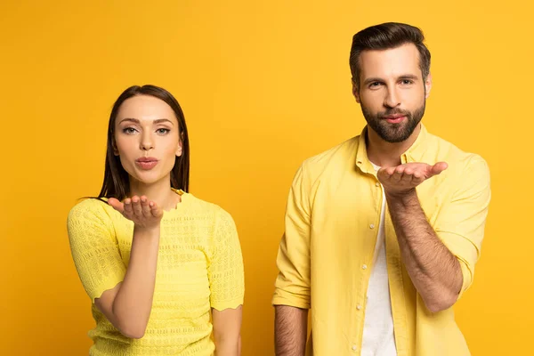 Junges Paar bläst Luftkuss auf gelbem Hintergrund — Stockfoto