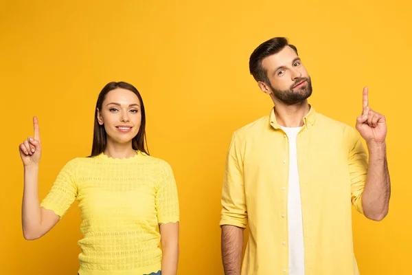 Jeune couple souriant pointant avec les doigts sur fond jaune — Photo de stock