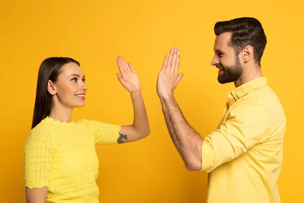 Jovem casal sorridente alta cinco no fundo amarelo — Fotografia de Stock