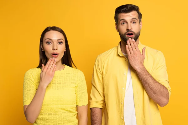 Schockiertes junges Paar blickt in Kamera auf gelbem Hintergrund — Stockfoto
