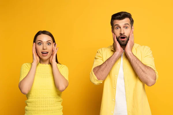 Surpris jeune couple regardant la caméra sur fond jaune — Photo de stock