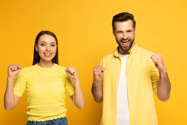 Cheerful couple showing yeah gesture at camera on yellow background — Stock Photo