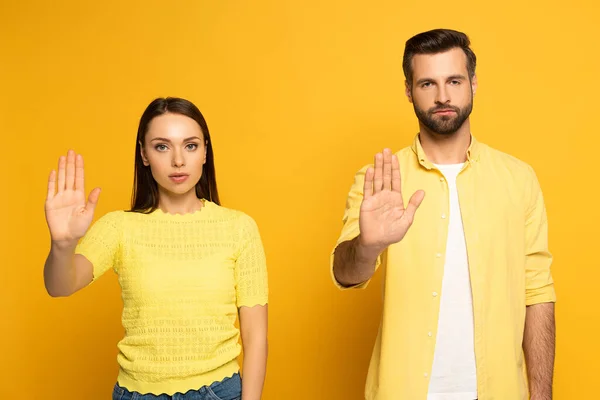 Jeune couple montrant geste d'arrêt à la caméra sur fond jaune — Photo de stock