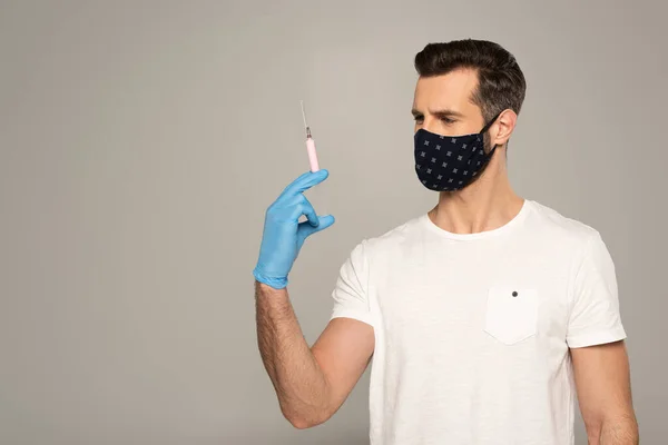 Homem de máscara de segurança e luva de látex segurando seringa isolada em cinza — Fotografia de Stock