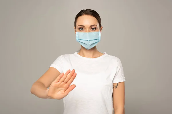 Frau mit medizinischer Maske zeigt Stopp-Geste isoliert auf grau — Stockfoto