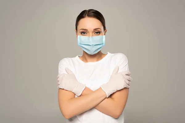 Mujer en máscara médica con brazos cruzados mirando a la cámara aislada en gris - foto de stock