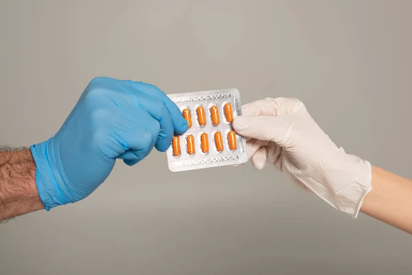 Vista recortada de pareja en guantes de látex sosteniendo ampolla con pastillas aisladas en gris - foto de stock