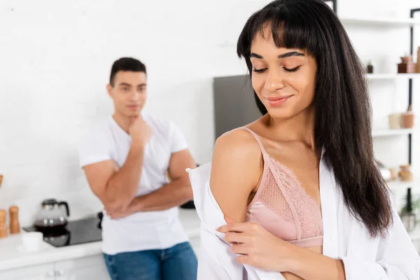 Enfoque selectivo del hombre con chica afroamericana sonriendo y quitándose la camisa en la cocina - foto de stock