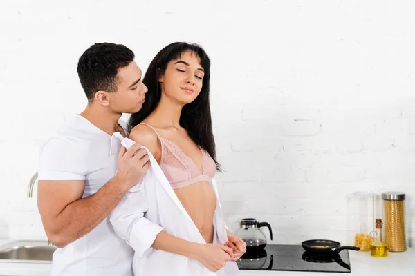 Uomo spogliarsi ragazza afro-americana con gli occhi chiusi in cucina — Foto stock