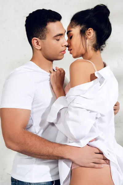 Interracial couple hugging and kissing with closed eyes on white — Stock Photo