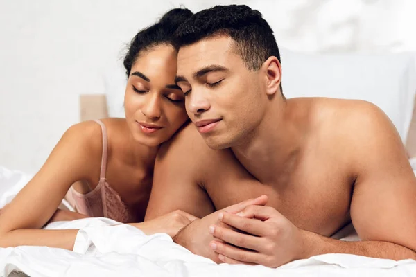 Couple interracial avec les yeux fermés couché sur le lit dans la chambre — Photo de stock