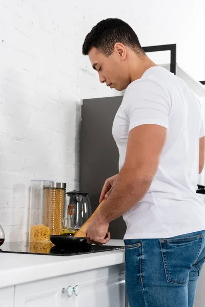 Mann kocht mit Pfanne und Spachtel in der Nähe von Küchenherd — Stockfoto