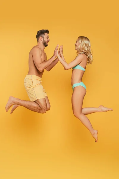 Vue latérale de jeune couple lévitant avec les mains jointes sur fond jaune — Photo de stock