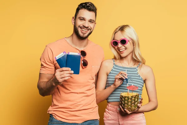 Felice uomo in possesso di documenti vicino sorridente ragazza con cocktail in ananas su sfondo giallo — Foto stock