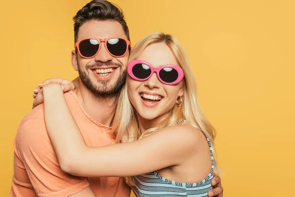 Glücklich schöner Mann und attraktive blonde Frau mit Sonnenbrille umarmen isoliert auf gelb — Stockfoto