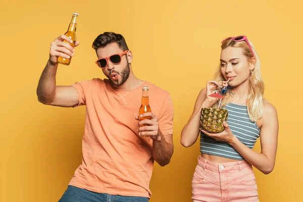 Uomo eccitato con bottiglie di birra vicino ragazza bionda bere cocktail da ananas su sfondo giallo — Foto stock