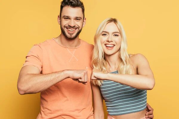 Heureux jeune couple souriant et caméra tout en tenant le poing pour poing sur fond jaune — Photo de stock
