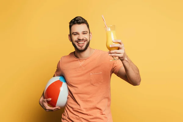Feliz joven sosteniendo inflatabe bola y vaso de jugo de naranja sobre fondo amarillo - foto de stock