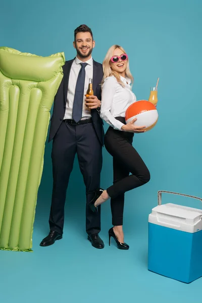 Happy businesspeople with drinks, inflatable mattress and portable fridge on blue background — Stock Photo