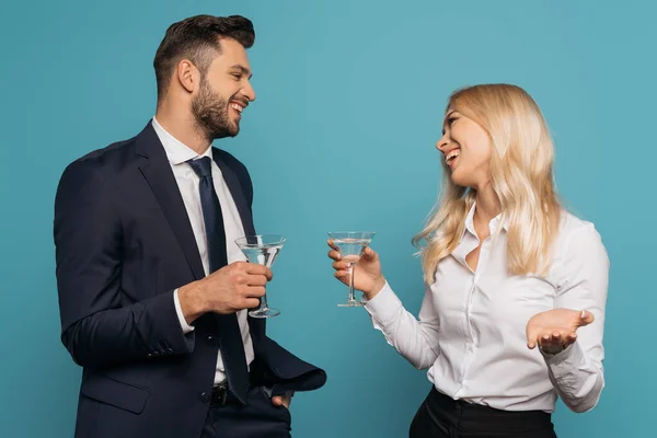 Happy businessman and businesswoman holding cocktail glasses while smiling at each other isolated on blue — Stock Photo