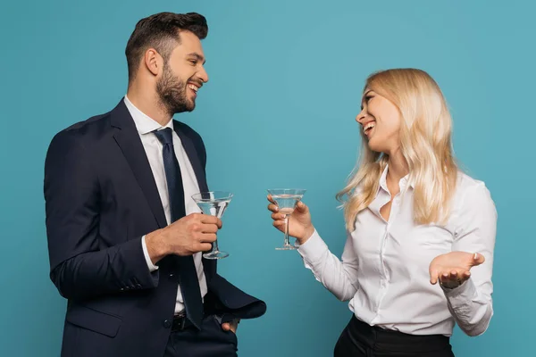 Happy businessman and businesswoman holding cocktail glasses while smiling at each other isolated on blue — Stock Photo