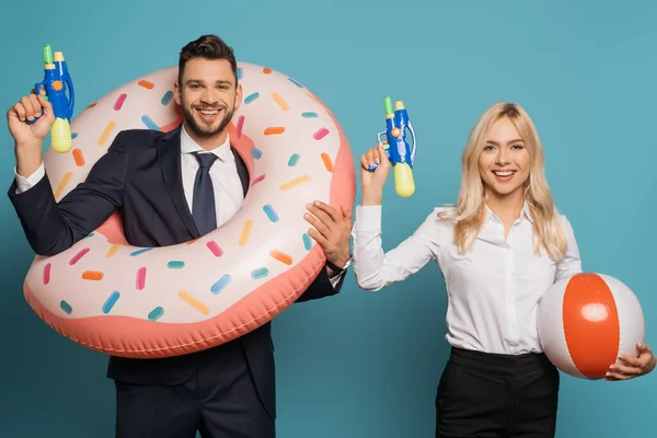 Happy businesspeople with swim ring and inflatable ball holding water guns on blue background — Stock Photo