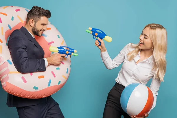 Alegres empresarios con anillo de natación y bola inflable que se divierten con pistolas de agua de juguete sobre fondo azul - foto de stock