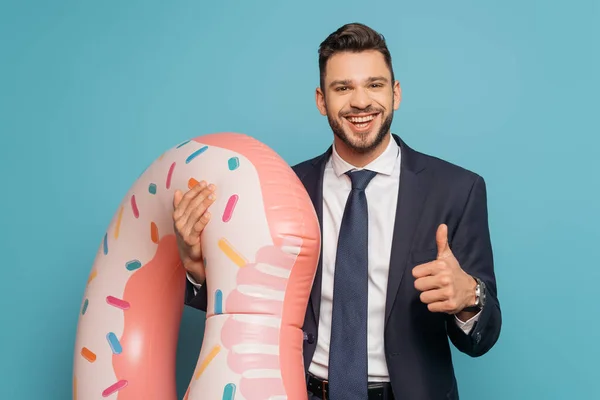 Glücklicher Geschäftsmann zeigt Daumen nach oben, während er aufblasbaren Ring auf blauem Hintergrund hält — Stockfoto