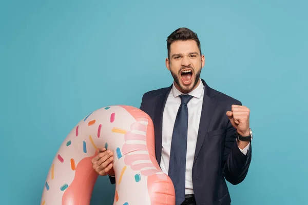 Aufgeregter Geschäftsmann zeigt Ja-Geste und schreit, während er einen aufblasbaren Ring auf blauem Hintergrund hält — Stockfoto