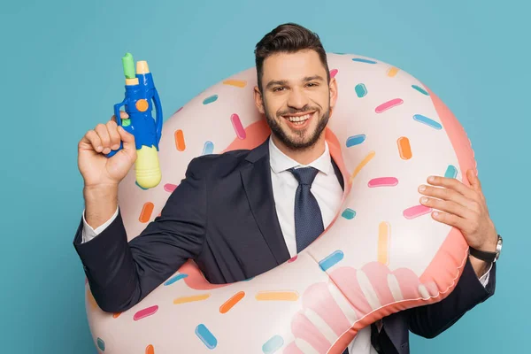 Alegre hombre de negocios en anillo de natación sosteniendo pistola de agua sobre fondo azul - foto de stock