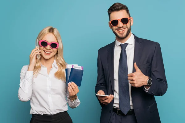 Щаслива бізнес-леді розмовляє на смартфоні, тримаючи документи біля усміхненого бізнесмена, показуючи великий палець на синьому фоні — Stock Photo