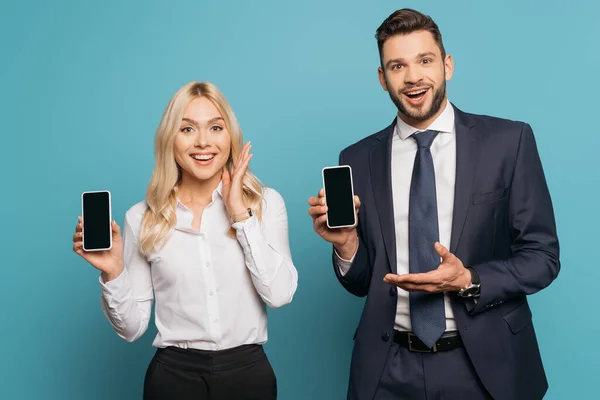 Homme d'affaires souriant et femme d'affaires montrant smartphones avec écran blanc sur fond bleu — Photo de stock