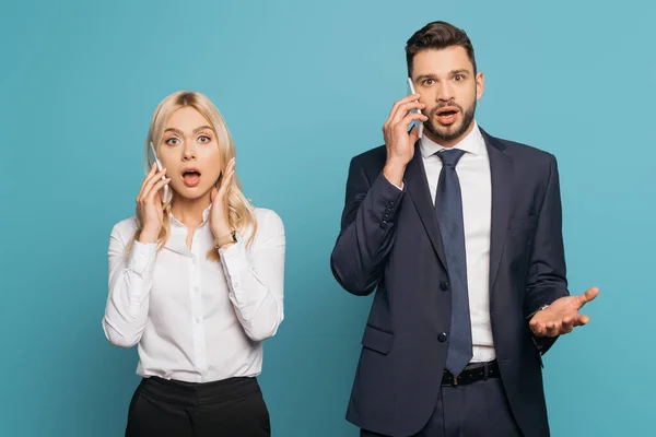 Шокированный бизнесмен и деловая женщина разговаривают на смартфонах на синем фоне — стоковое фото