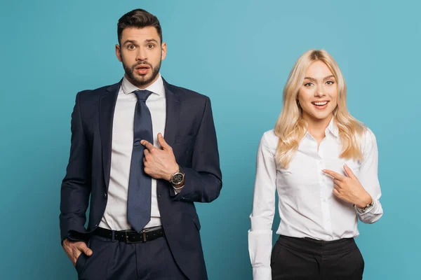 Homme d'affaires surpris et femme d'affaires pointant avec les doigts sur eux-mêmes sur fond bleu — Photo de stock