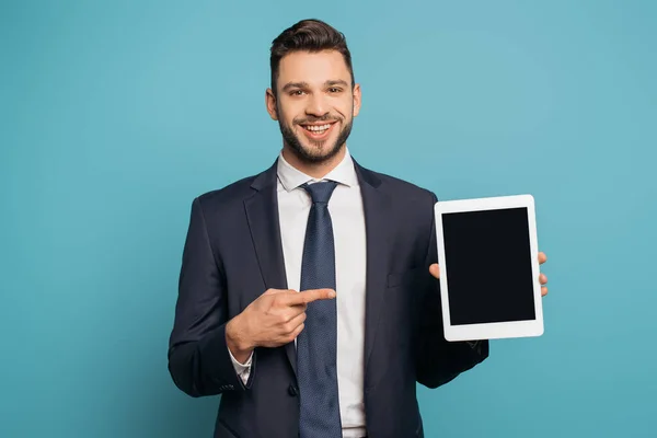 Hombre de negocios feliz apuntando con el dedo al teléfono inteligente con pantalla en blanco sobre fondo azul - foto de stock