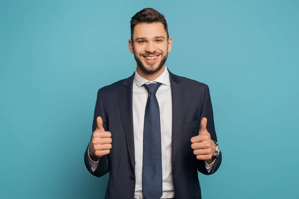 Homem de negócios feliz mostrando polegares para cima enquanto olha para a câmera no fundo azul — Fotografia de Stock