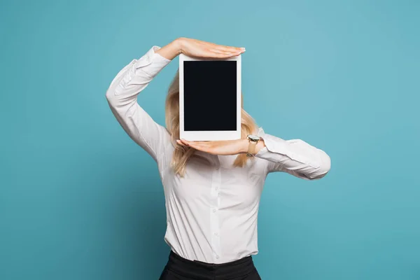 Geschäftsfrau in weißer Bluse verdeckt Gesicht mit digitalem Tablet mit leerem Bildschirm auf blauem Hintergrund — Stockfoto