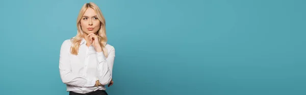 Panoramische Ernte verträumter Geschäftsfrau, die die Hand am Kinn hält, während sie auf blauem Hintergrund wegschaut — Stockfoto