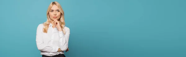 Panoramic crop of dreamy businesswoman holding hand near chin while looking away on blue background — Stock Photo