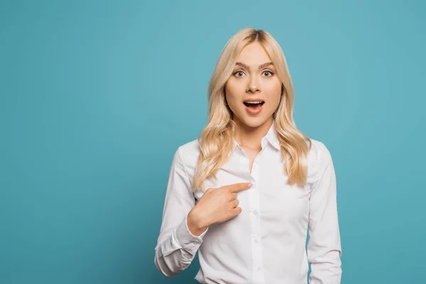 Surprised businesswoman pointing with finger at herself while looking at camera on blue background — Stock Photo