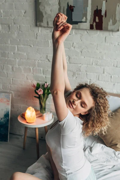 Beautiful girl stretching in cozy bedroom with Himalayan salt lamp — Stock Photo