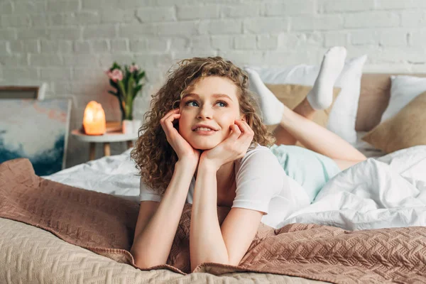 Dreamy woman in homewear lying on bed in bedroom with Himalayan salt lamp — Stock Photo
