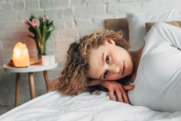 Attractive woman lying on bed in bedroom with Himalayan salt lamp — Stock Photo