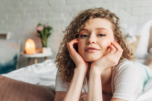 Curly girl in homewear lying on bed in bedroom with Himalayan salt lamp — Stock Photo