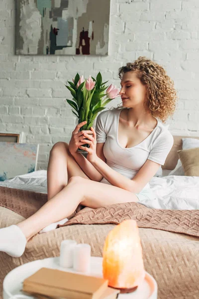 Schöne lockige Mädchen mit Blumen im Schlafzimmer mit Himalaya-Salzlampe — Stockfoto