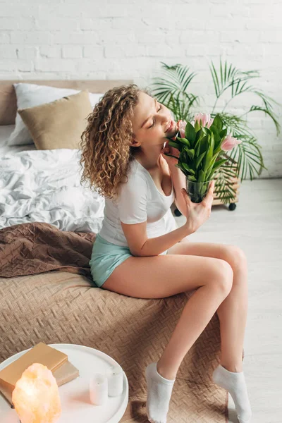 Happy curly girl holding tulips in bedroom with Himalayan salt lamp and books — Stock Photo