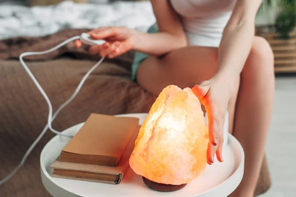 Перевернутий вид на молоду жінку, яка переключає гімалайську соляну лампу в спальні з книжками — стокове фото