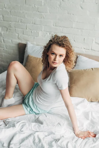 Attractive young woman in homewear sitting on bed in morning — Stock Photo